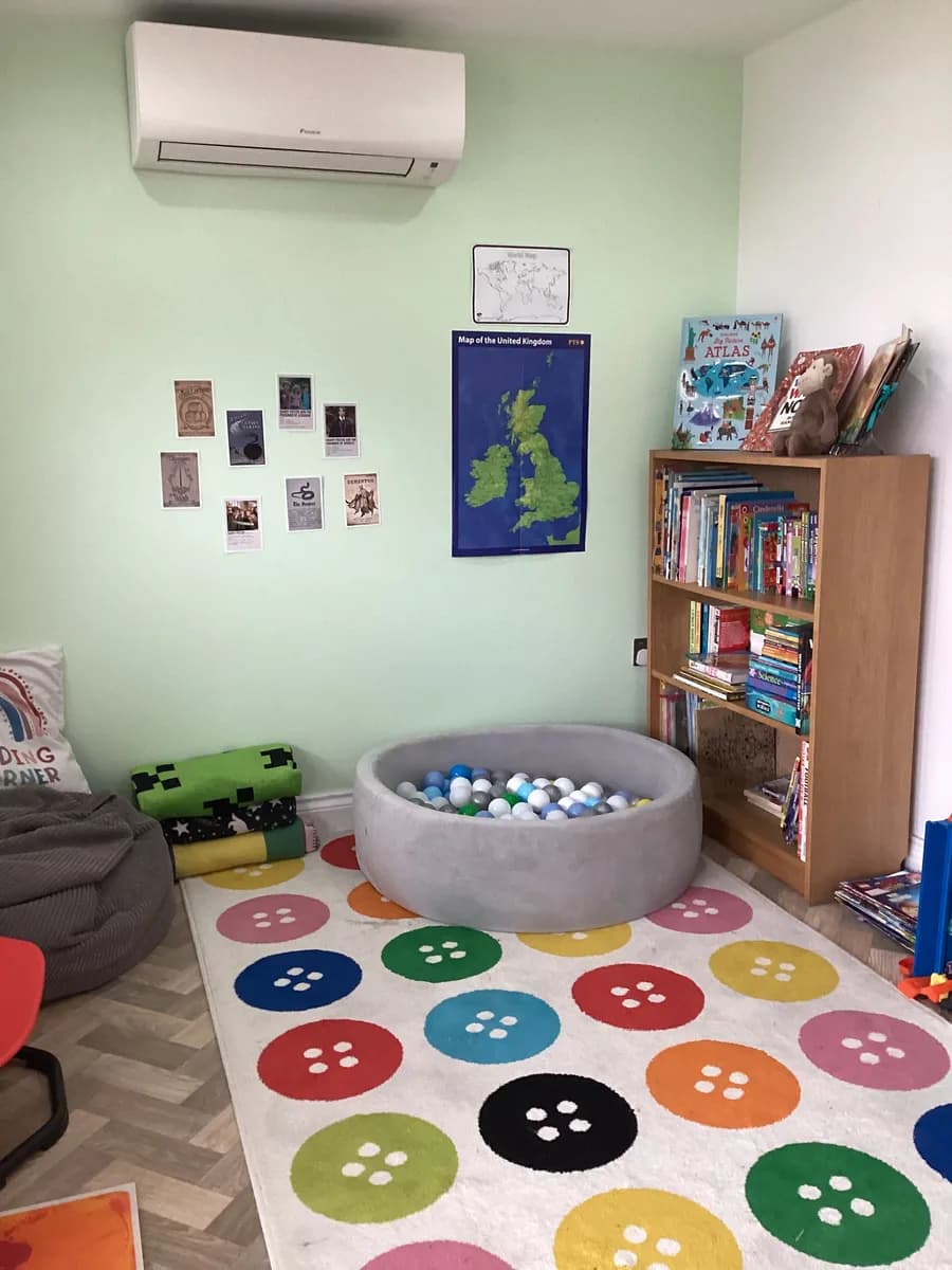 A grey ball pit beside a bookshelf and a rug patterned with colourful buttons