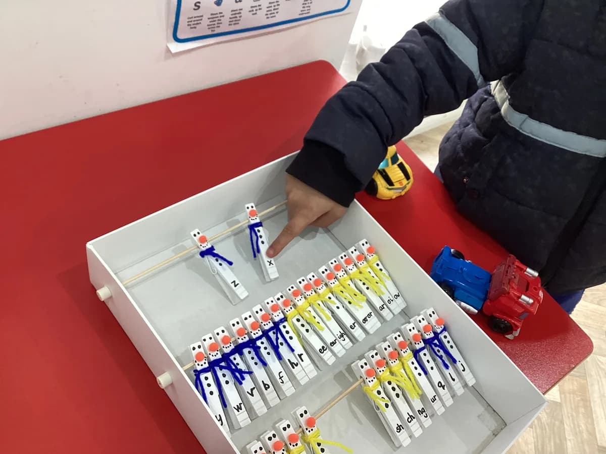 A child pointing to rows of phonics linking blocks in a tray