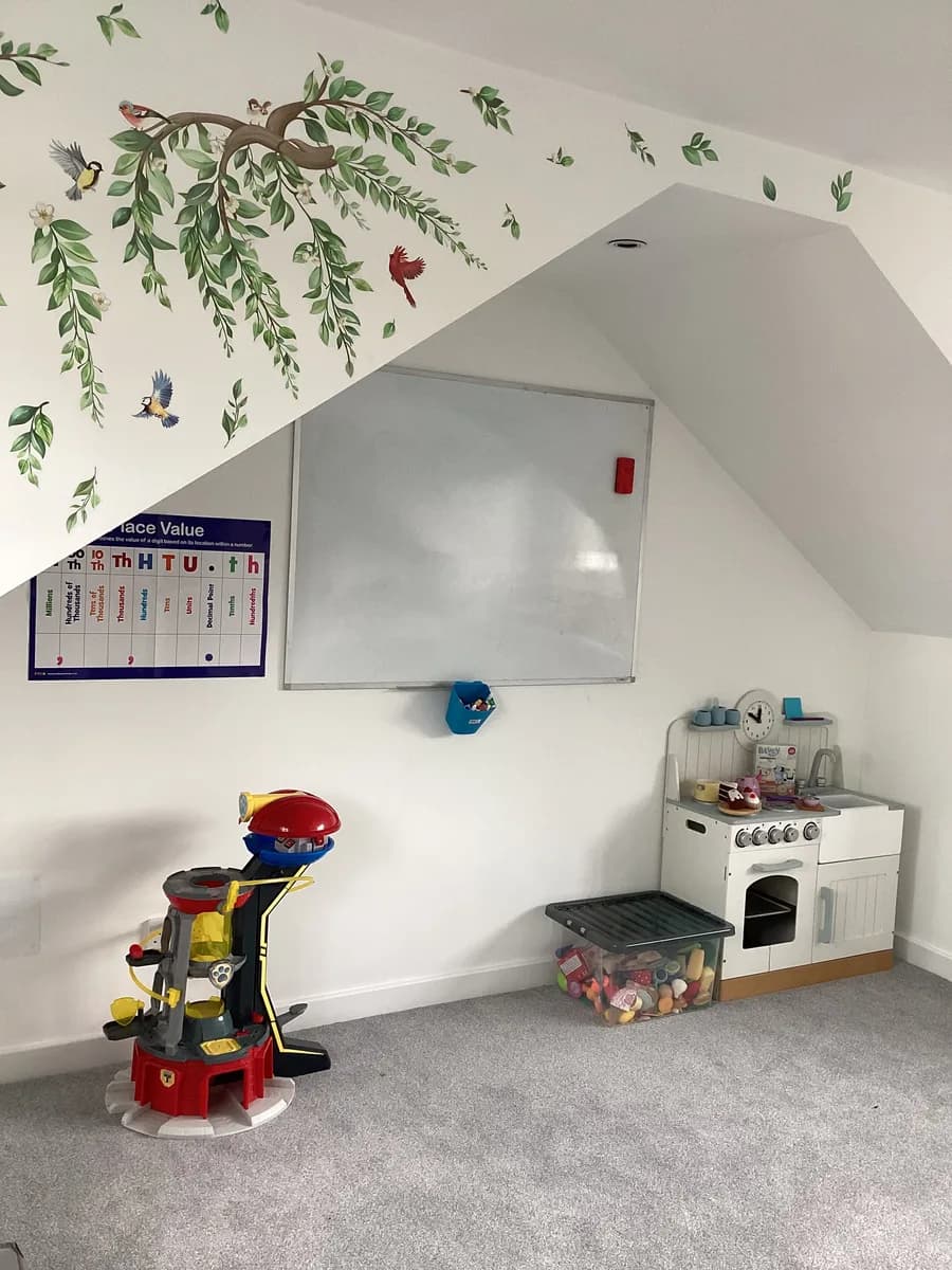 A play kitchen, toy garage and whiteboard beneath a leafy wall mural