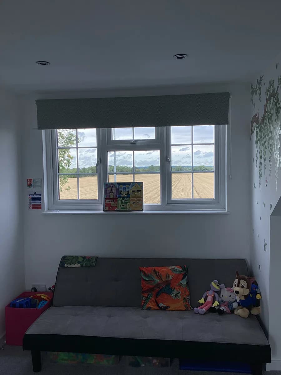 A grey sofa with soft toys beneath a window overlooking fields