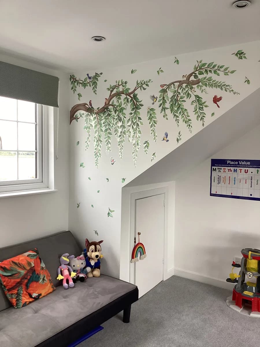 A grey sofa with cushions and soft toys beneath a woodland wall mural
